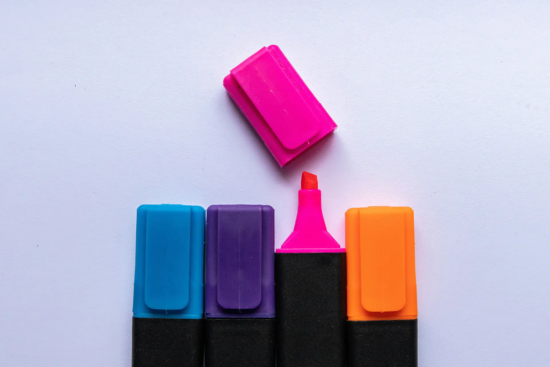 Four highlighters with blue, purple, pink, and orange caps, one pink uncapped showing red tip.