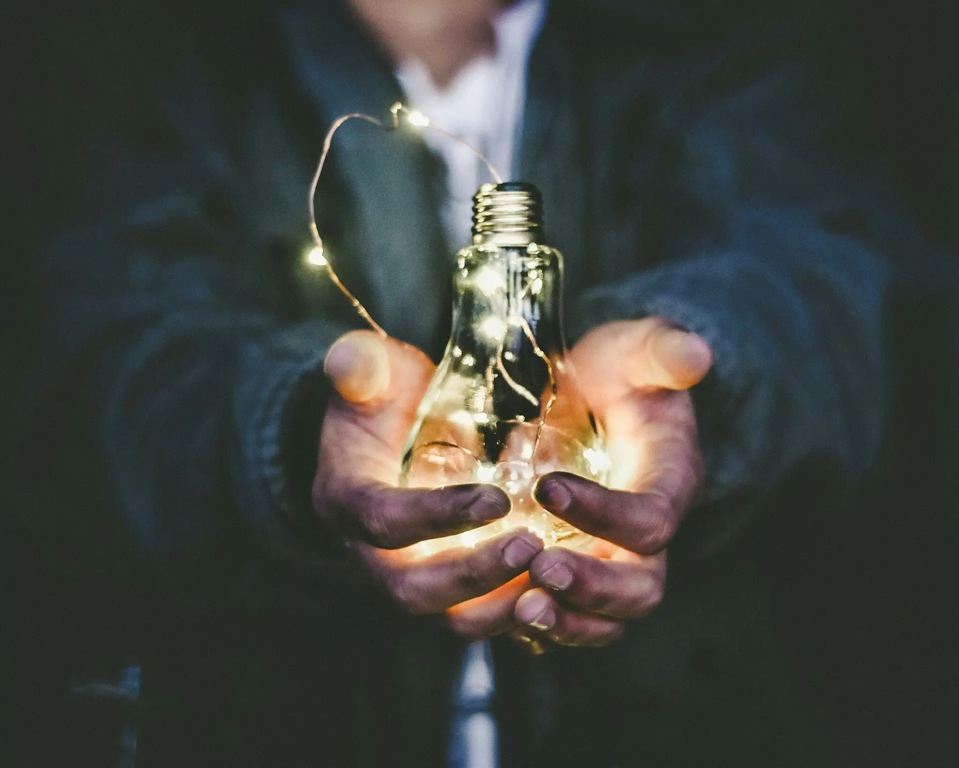 Person holding a glass light bulb filled with glowing string lights in both hands.